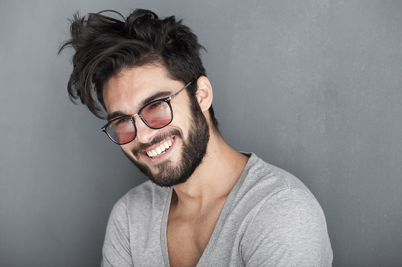 Sexy man with beard smiling big against wall